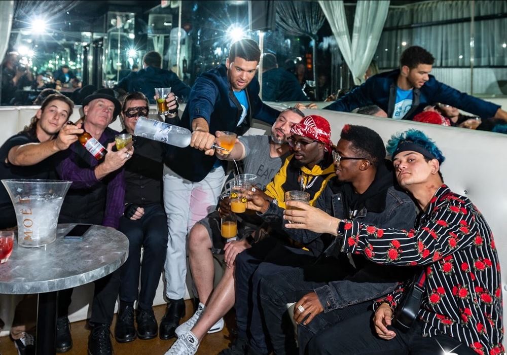 Bachelor party group enjoying VIP bottle service in a club, with one man from the group pouring vodka.