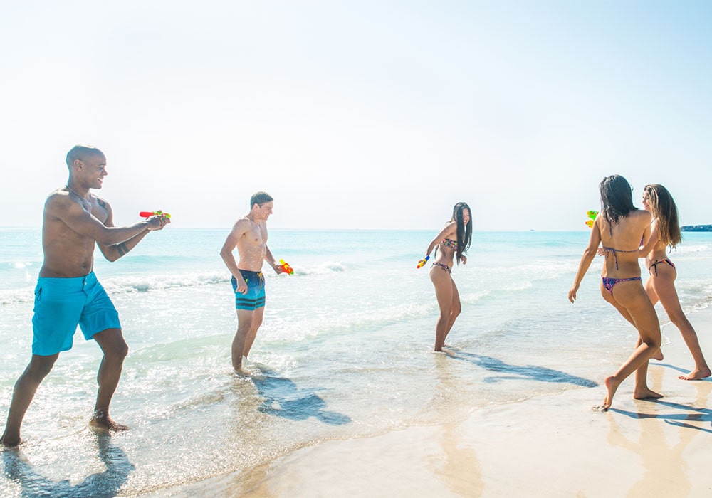 Group of young adults playing with water guns at the beach.