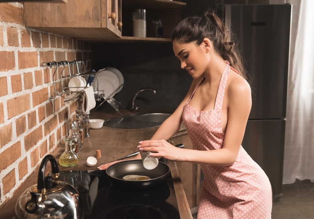 Sexy brunette wearing an apron cooking eggs in a kitchen.