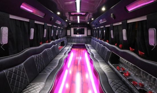 Spacious party bus interior with black leather seating, vibrant purple lighting, and sleek modern design.