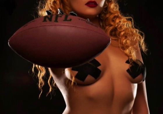 Young woman with long curly blonde hair holding an NFL football, wearing black tape in an 'X' shape over chest.