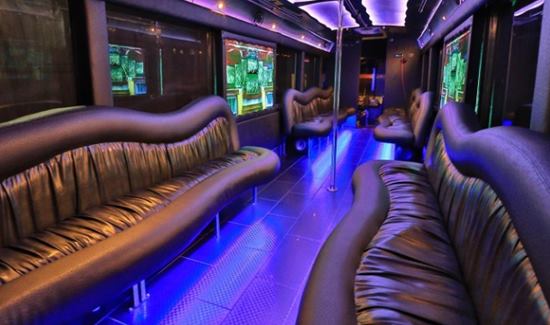 Party bus interior with wavy black leather seating, blue and purple LED lighting, and dance poles.