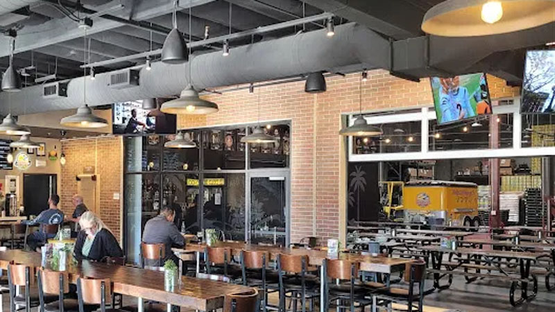 Modern Palm Springs brewery interior with wooden tables, relaxed atmosphere, a few customers, and sports on TV.
