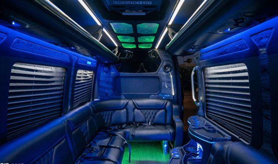 Luxury party bus interior with comfortable black leather seating and blue and green lighting.