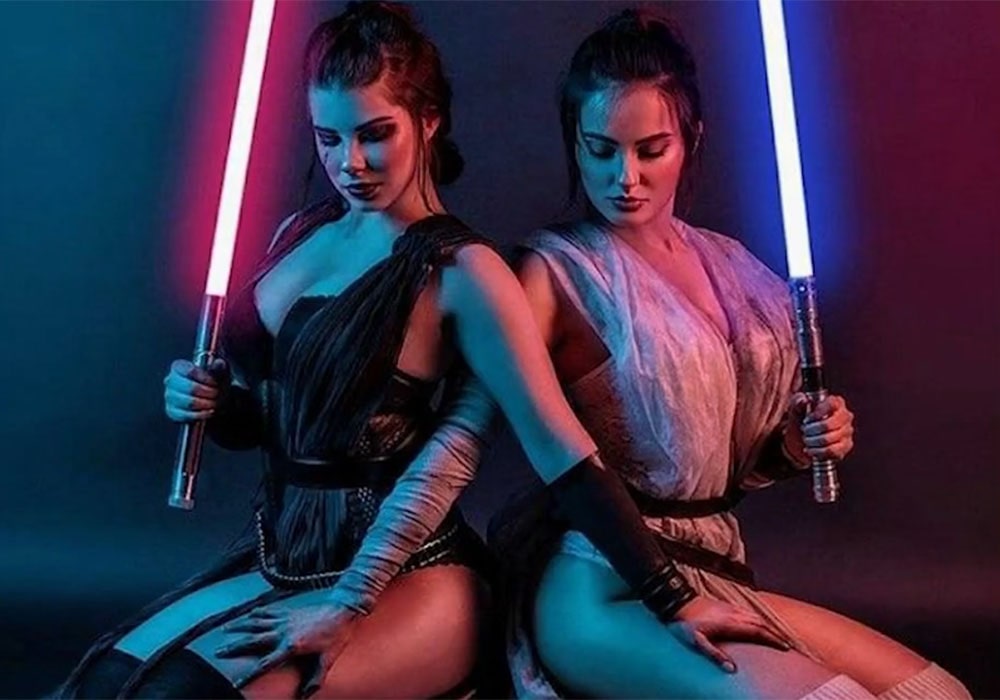 Two female entertainers dressed in stylized costumes inspired by Star Wars characters, each holding a lightsaber.