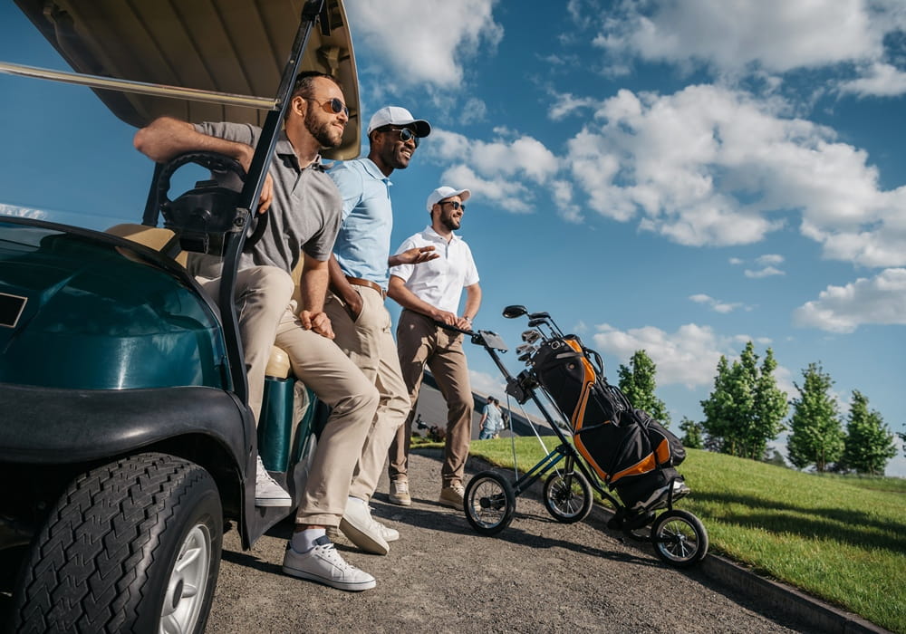 Three guys posing on the golf course with a golf cart.