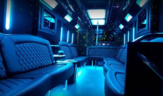 Limo bus interior with leather couches, blue floor lights, and a dance pole.