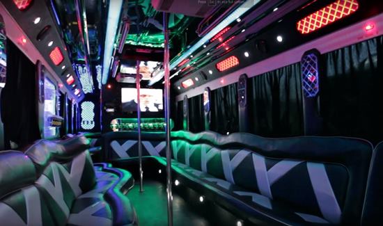 Colorful party bus interior with patterned leather seating, vibrant LED lights, and a central dance pole.